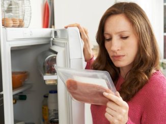 Woman looking at label of lunch meat with fridge open