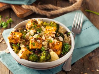 Tofu, broccoli, rice, almonds and other gluten-free foods in a bowl on top of a napkin on a wood table