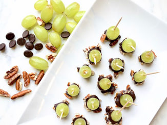 Grapes dipped in dark chocolate and pecans with toothpicks on white plate