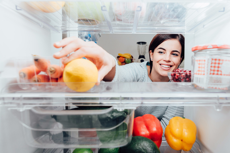 Women reaching into back of fridge to grab lemon