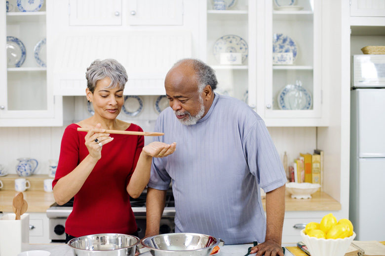Older couple cooking and tasting dishes together in a kitchen