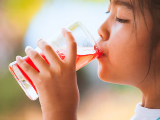 Little child girl drinking red juice water with ice from glass