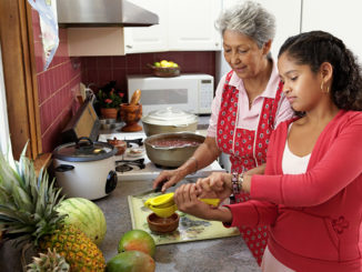 Family in kitchen, grandmother watching granddaughter (10-12) squeezing lime