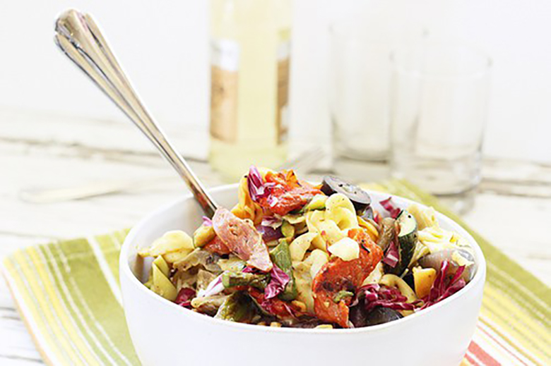 Grilled Vegetable and Tortellini Antipasto Salad in a white bowl with serving spoon