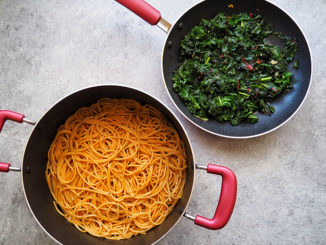 Greens in a pot and pasta in a larger two-handled pot, shot from above