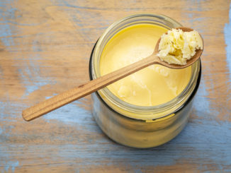 jar and spoon of ghee (clarified butter) on grunge wood - top view