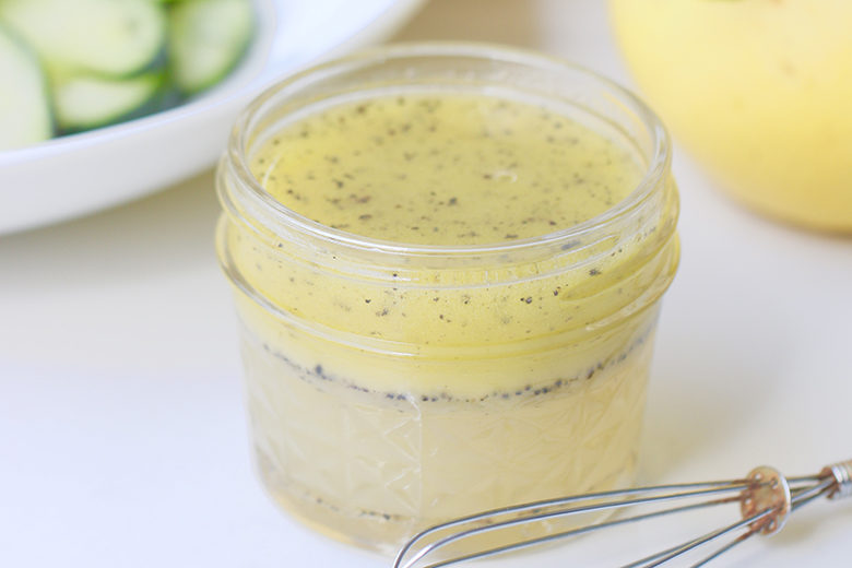 Lemon poppyseed dressing in a small mason jar with whisk and lemons and cucumbers in background