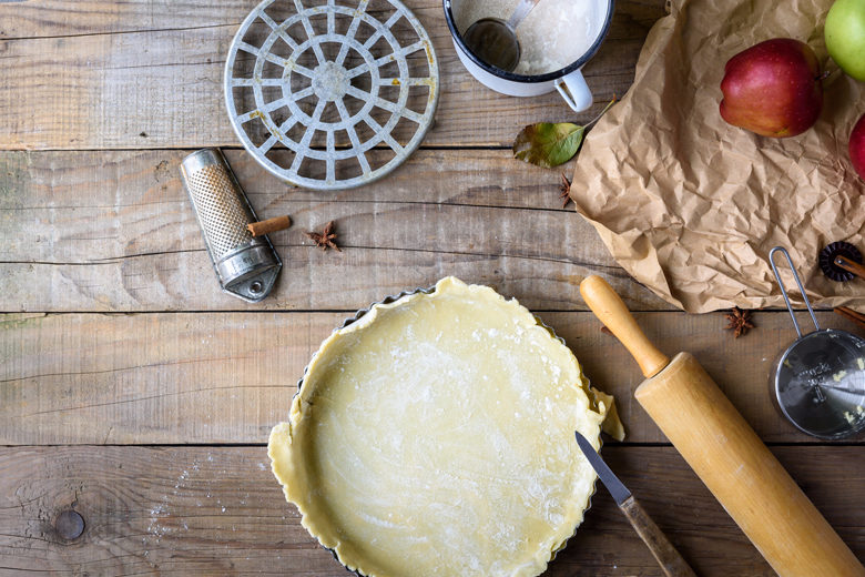 Empty unbaked crust surrounded by tools for baking a pie