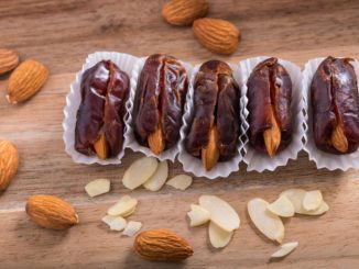 Dates stuffed with almonds lined up on wooden background with almonds scattered around