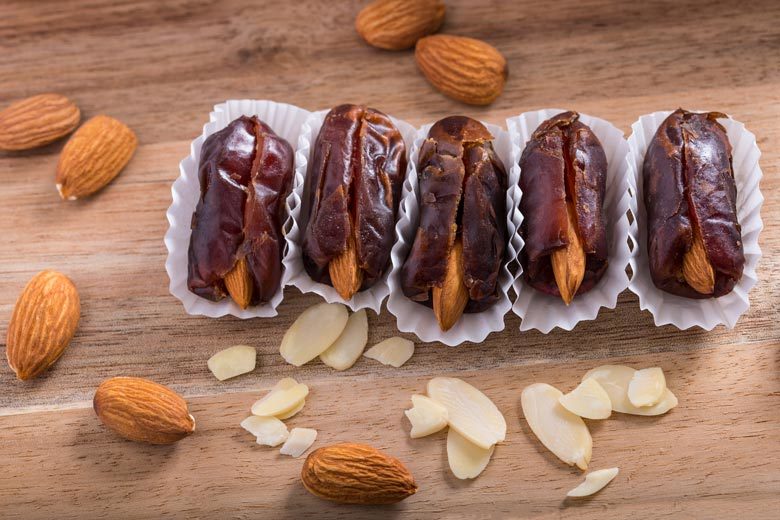Dates stuffed with almonds lined up on wooden background with almonds scattered around