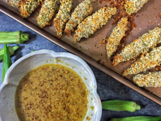 A baking tray of oven baked okra next to a bowl of honey dijon dipping sauce