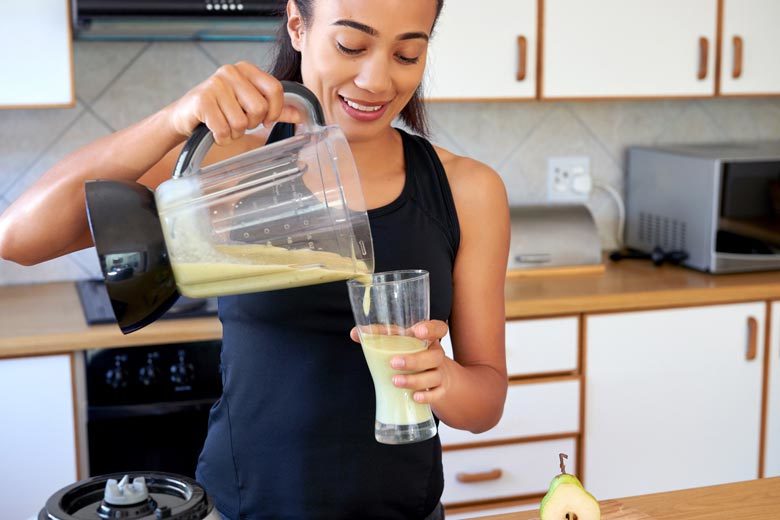 Woman in workout gear pouring herself a smoothie milkshake